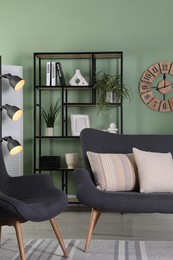 Photo of Comfortable sofa with pillows, armchair, shelving unit and houseplants in room