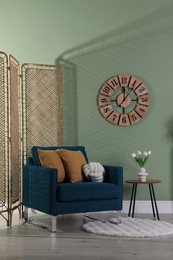 Folding screen, comfortable armchair with pillows and side table in room