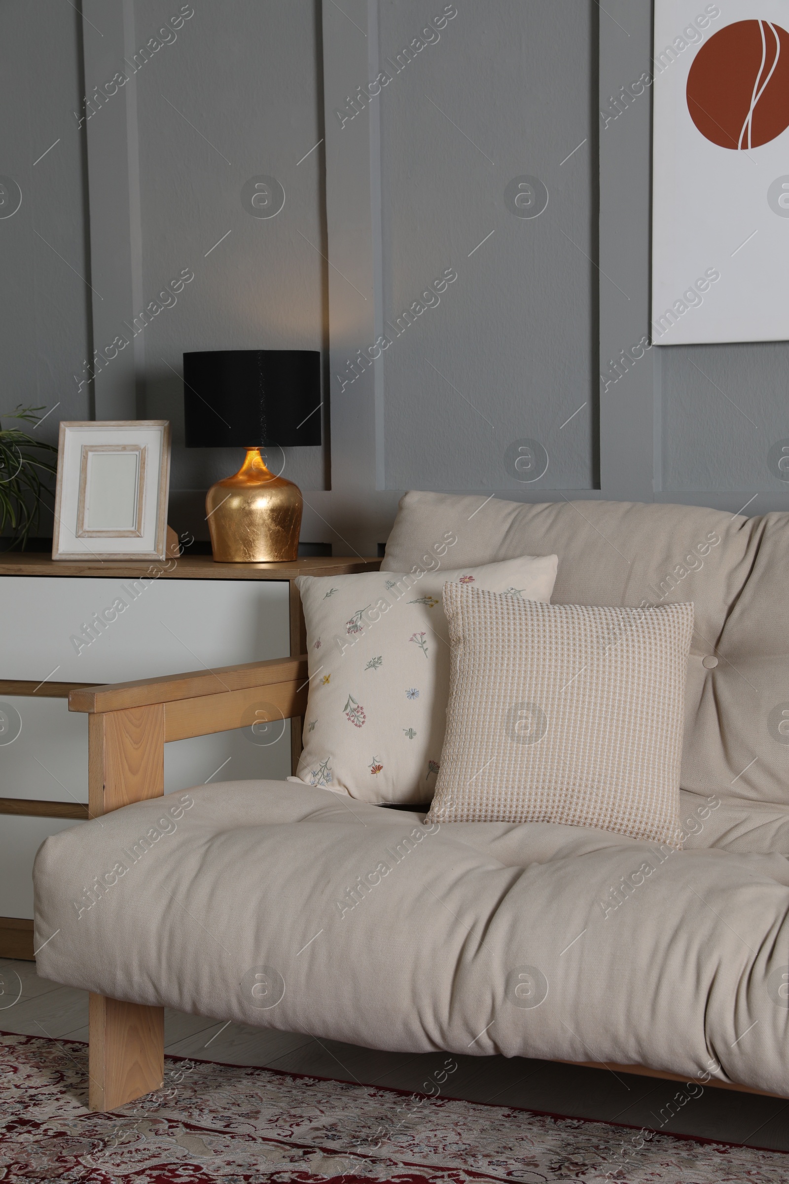 Photo of Comfortable sofa with pillows and chest of drawers in room