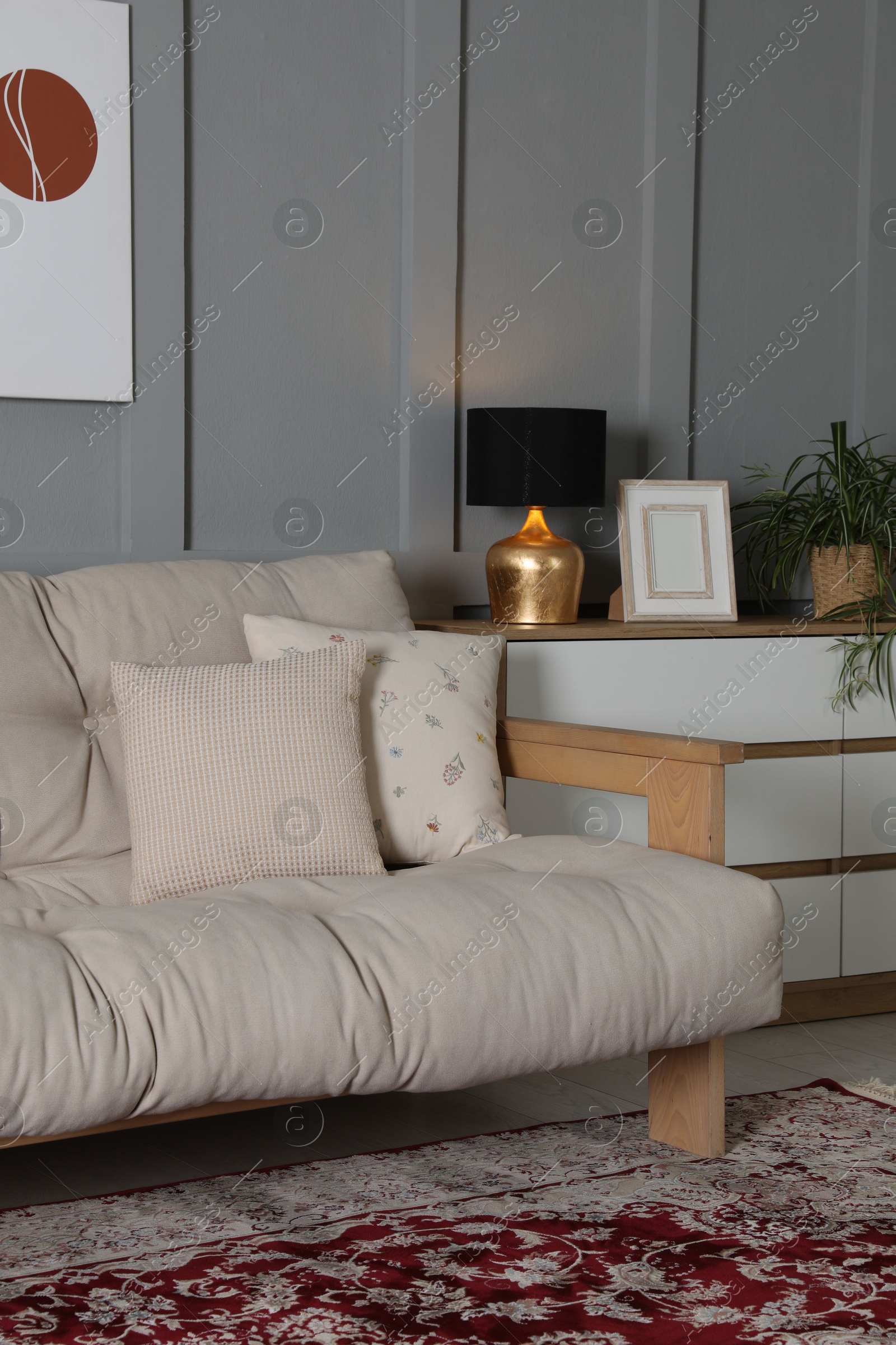 Photo of Comfortable sofa with pillows and chest of drawers in room