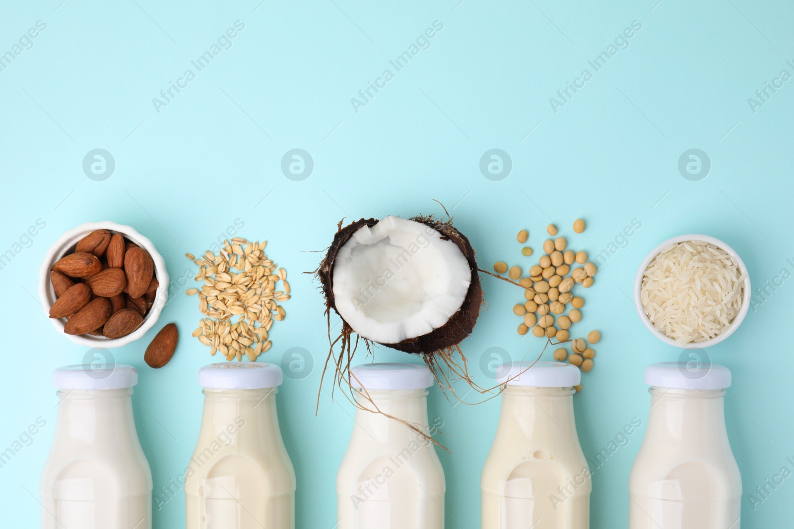 Photo of Different types of vegan milk in bottles and ingredients on light blue table, flat lay. Space for text