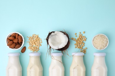 Different types of vegan milk in bottles and ingredients on light blue table, flat lay. Space for text