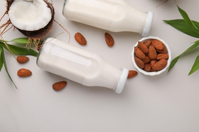 Photo of Different types of vegan milk in bottles with ingredients and green leaves on light grey table, flat lay. Space for text