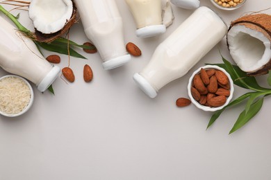 Photo of Different types of vegan milk in bottles with ingredients and leaves on light grey table, flat lay. Space for text