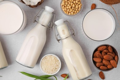 Photo of Different types of vegan milk with ingredients and leaves on light grey table, flat lay