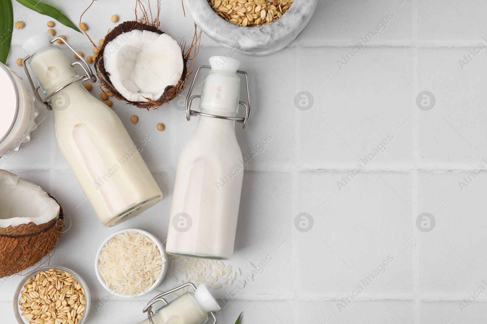 Photo of Different types of vegan milk in bottles and ingredients on white tiled table, flat lay. Space for text