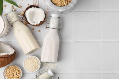 Photo of Different types of vegan milk in bottles and ingredients on white tiled table, flat lay. Space for text