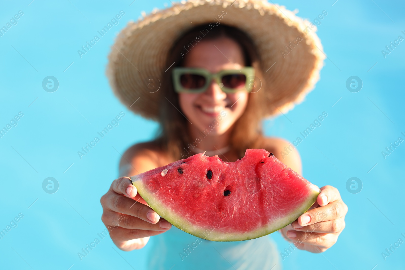 Photo of Happy woman with slice of juicy watermelon in swimming pool outdoors, selective focus