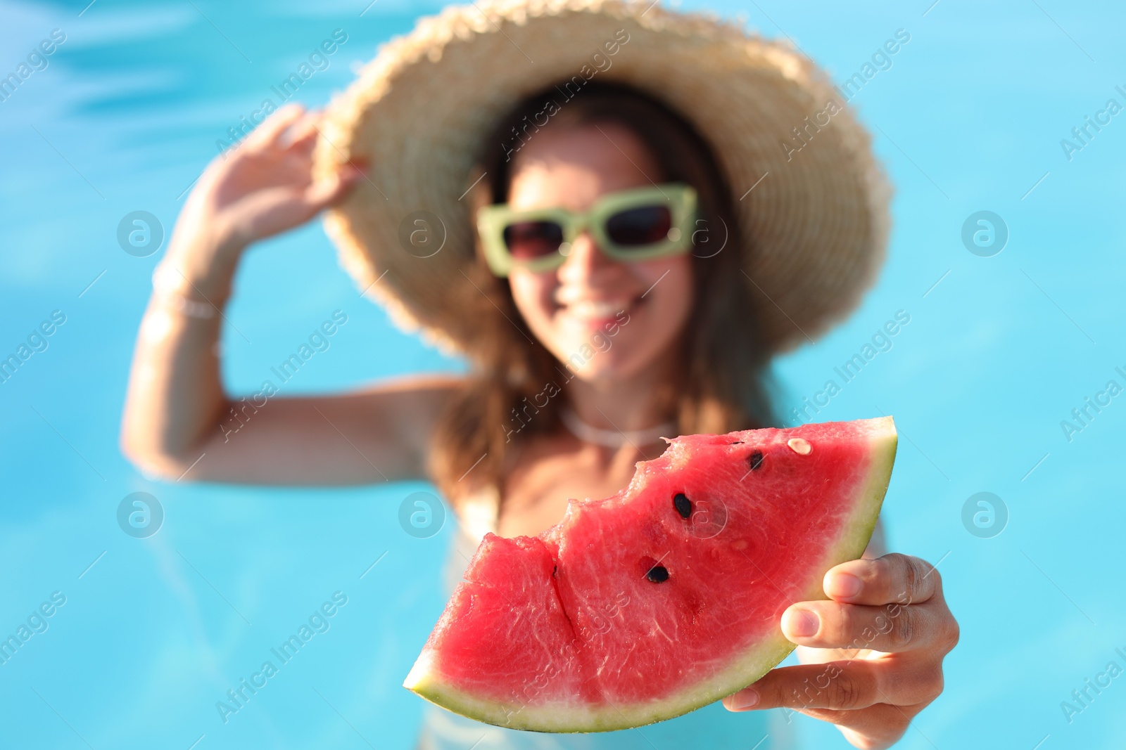 Photo of Happy woman with slice of juicy watermelon in swimming pool outdoors, selective focus