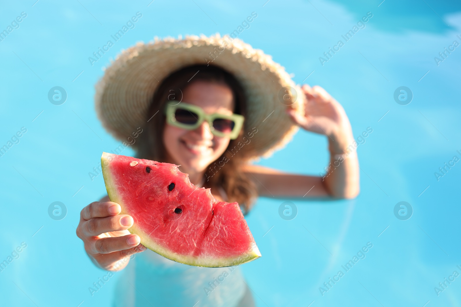 Photo of Happy woman with slice of juicy watermelon in swimming pool outdoors, selective focus