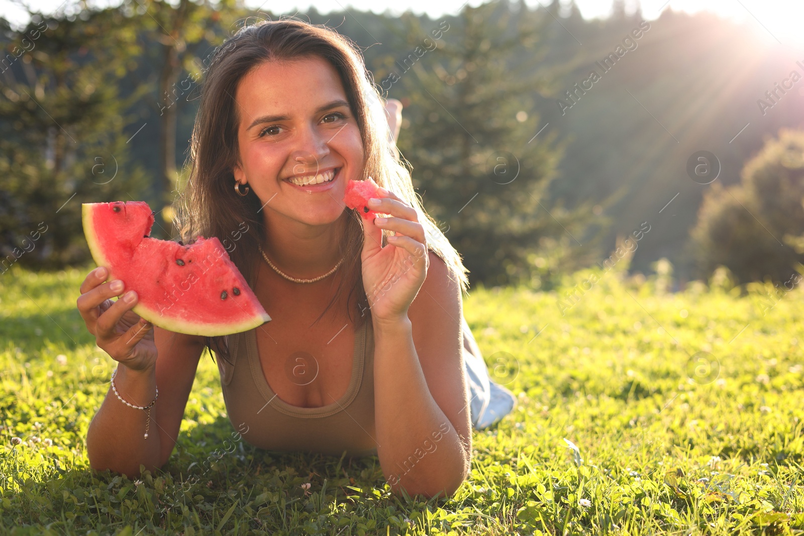 Photo of Happy woman with slice of juicy watermelon on green grass outdoors, space for text