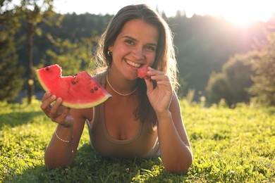 Happy woman eating juicy watermelon on green grass outdoors, space for text