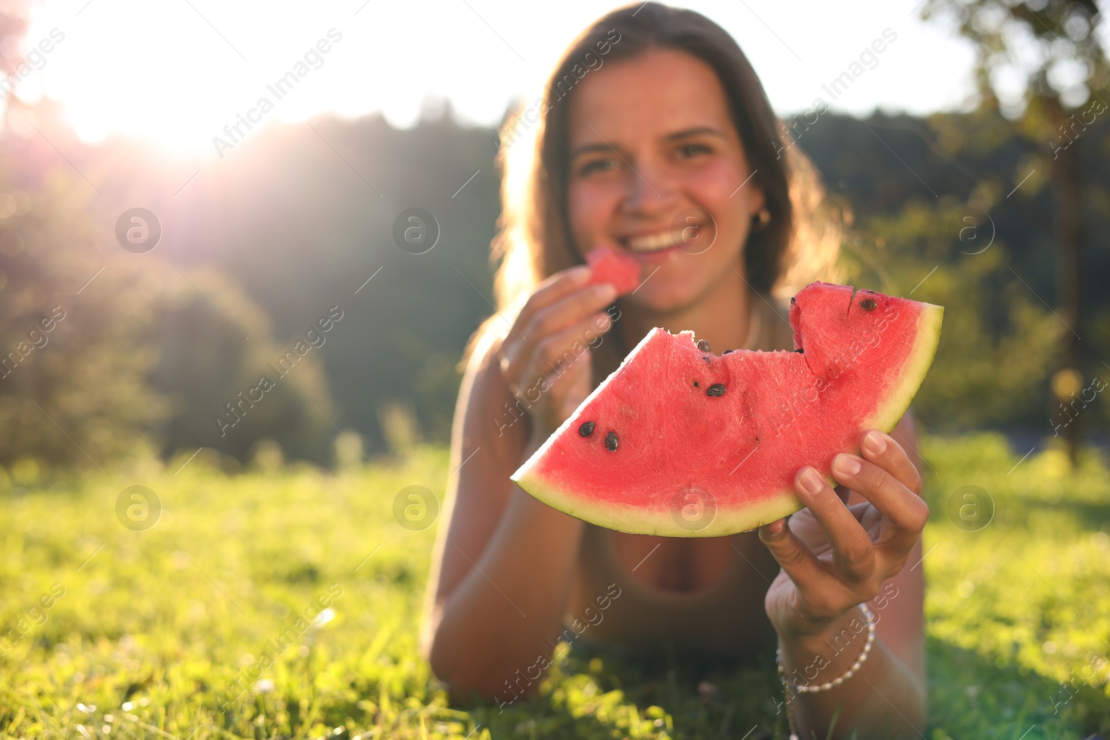 Photo of Happy woman with slice of juicy watermelon on green grass outdoors, space for text