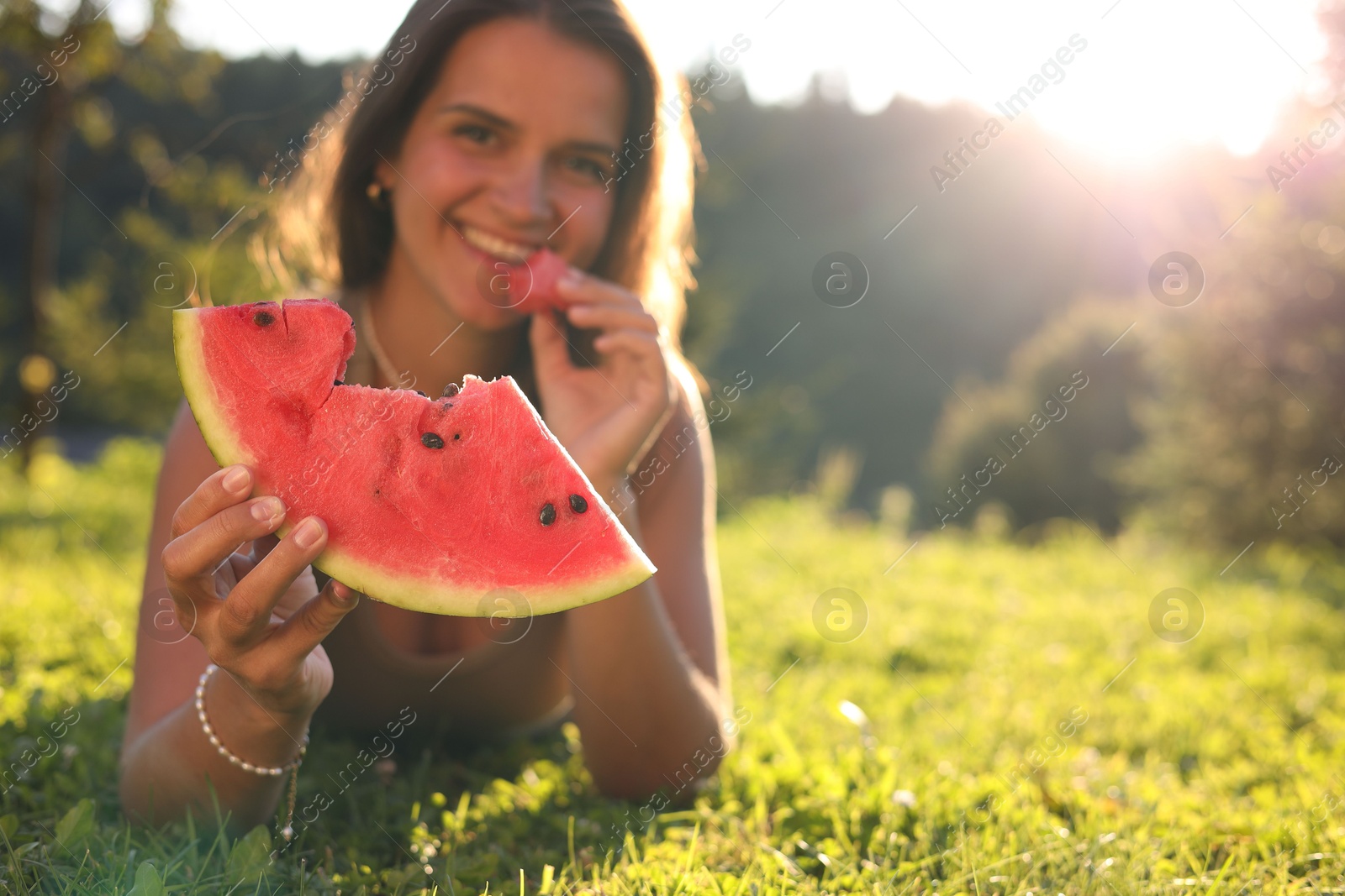 Photo of Happy woman with slice of juicy watermelon on green grass outdoors, space for text