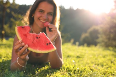 Happy woman with slice of juicy watermelon on green grass outdoors, space for text