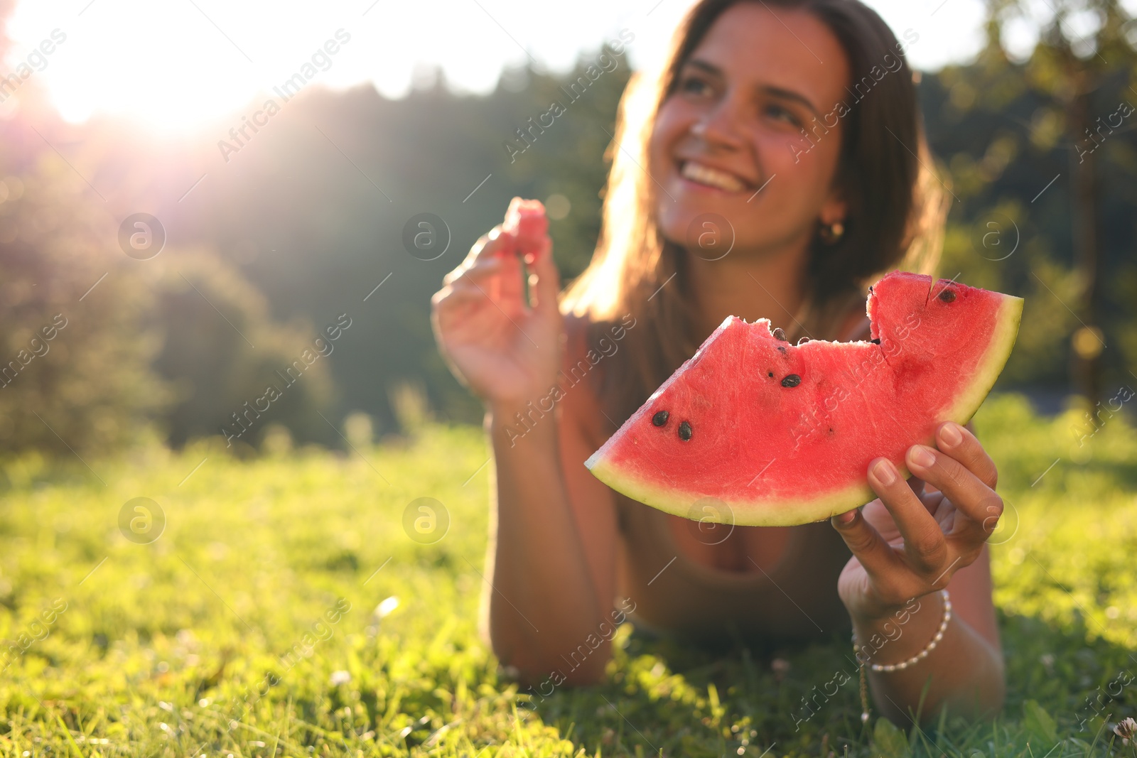 Photo of Happy woman with slice of juicy watermelon on green grass outdoors, space for text