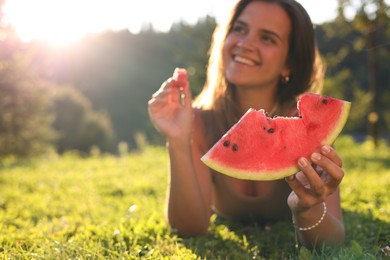 Happy woman with slice of juicy watermelon on green grass outdoors, space for text