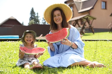 Mother and her daughter with slices of juicy watermelon on green grass outdoors