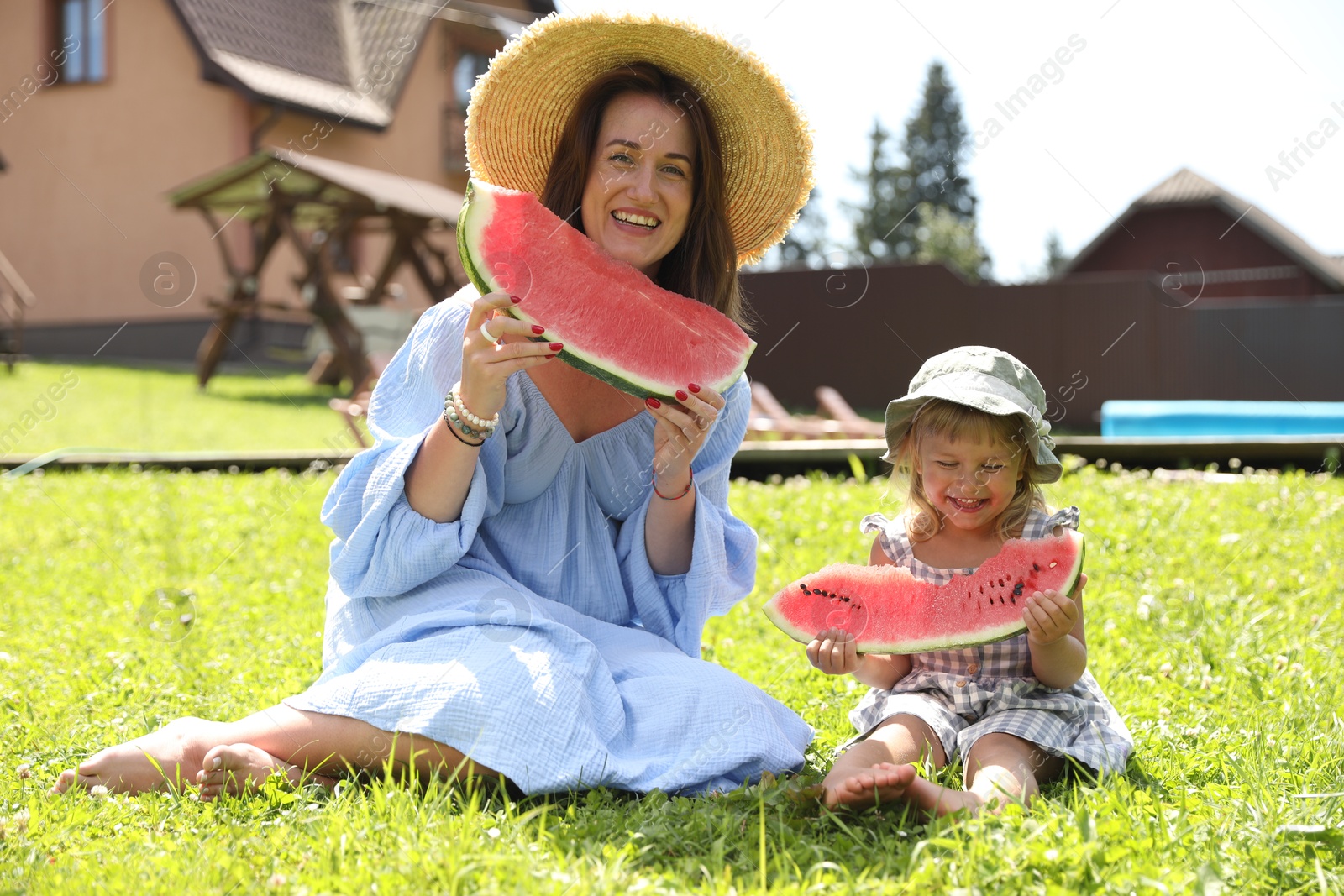 Photo of Mother and her daughter with slices of juicy watermelon on green grass outdoors