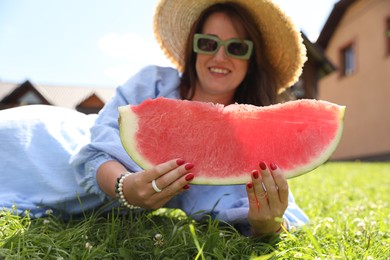 Woman with slice of juicy watermelon on green grass outdoors, selective focus