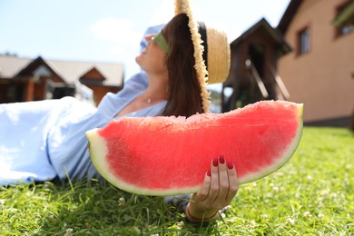 Photo of Woman with slice of juicy watermelon on green grass outdoors, selective focus