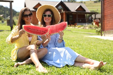 Photo of Happy women with slices of juicy watermelon on green grass outdoors