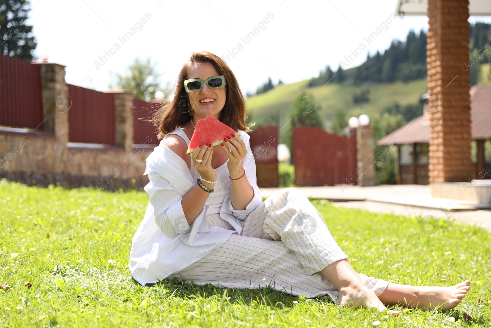 Photo of Happy woman holding slice of juicy watermelon on green grass outdoors