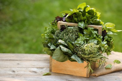 Different fresh herbs in basket on wooden table outdoors, space for text