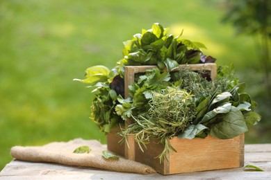 Photo of Different fresh herbs in basket on wooden table outdoors