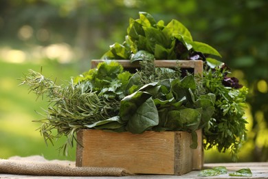 Photo of Different fresh herbs in basket on wooden table outdoors