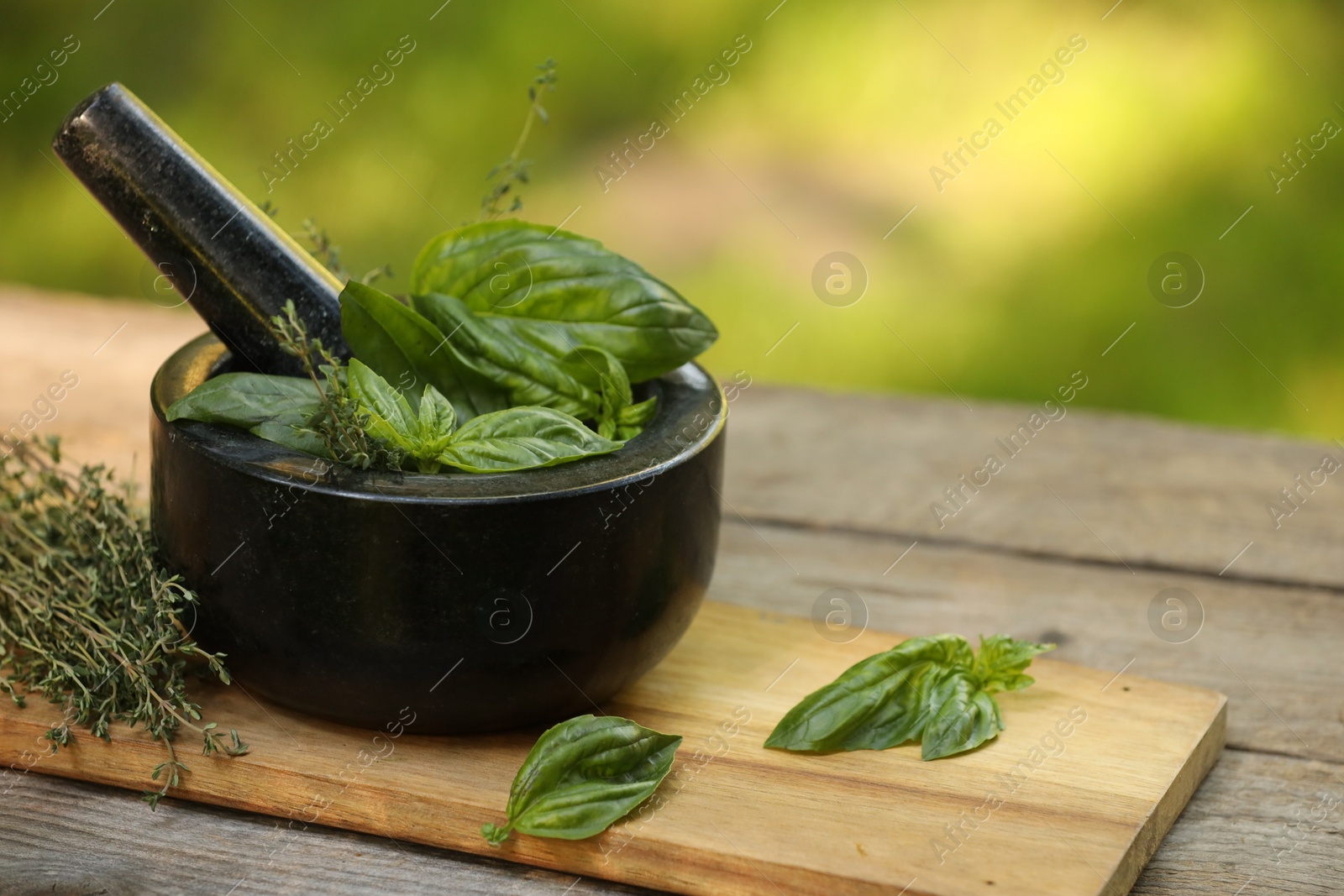 Photo of Fresh herbs. Basil leaves in mortar and thyme on wooden table outdoors, closeup. Space for text