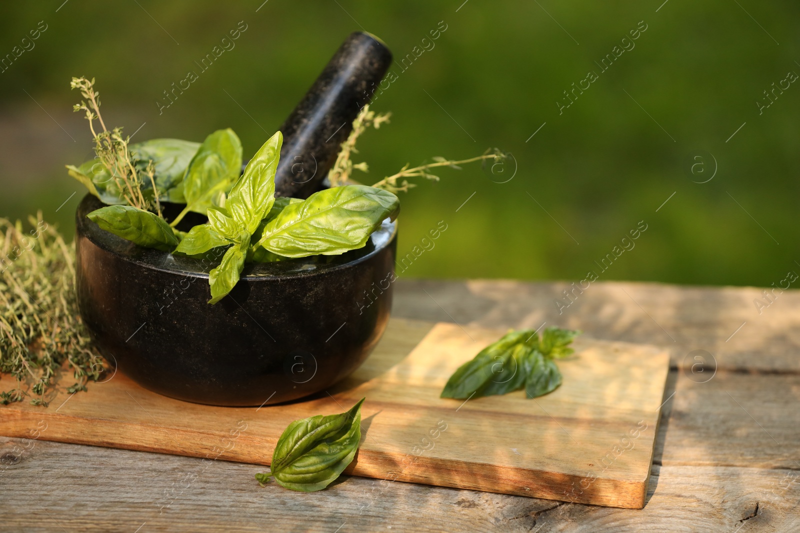 Photo of Fresh herbs. Basil leaves in mortar and thyme on wooden table outdoors, closeup. Space for text