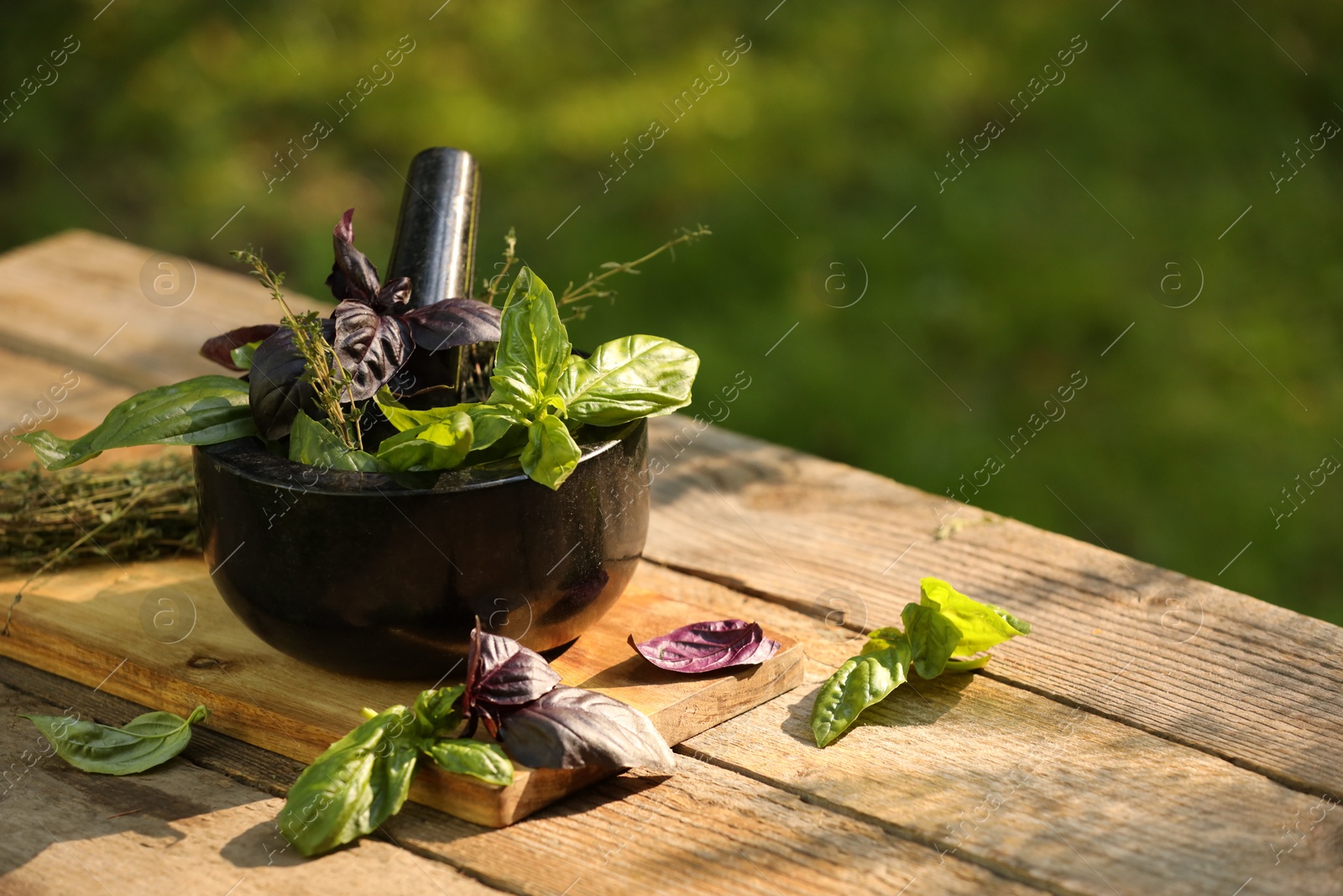 Photo of Fresh herbs. Different basil leaves in mortar on wooden table outdoors, space for text