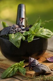 Photo of Fresh herbs. Different basil leaves in mortar on wooden table outdoors, closeup