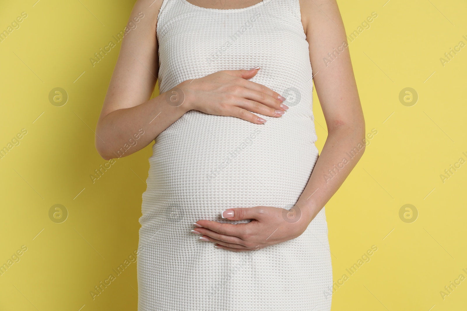 Photo of Young pregnant woman on yellow background, closeup