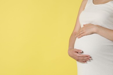 Photo of Young pregnant woman on yellow background, closeup. Space for text