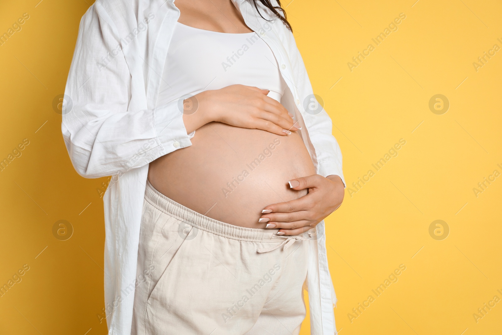 Photo of Young pregnant woman on yellow background, closeup. Space for text