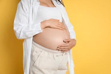 Photo of Young pregnant woman on yellow background, closeup. Space for text