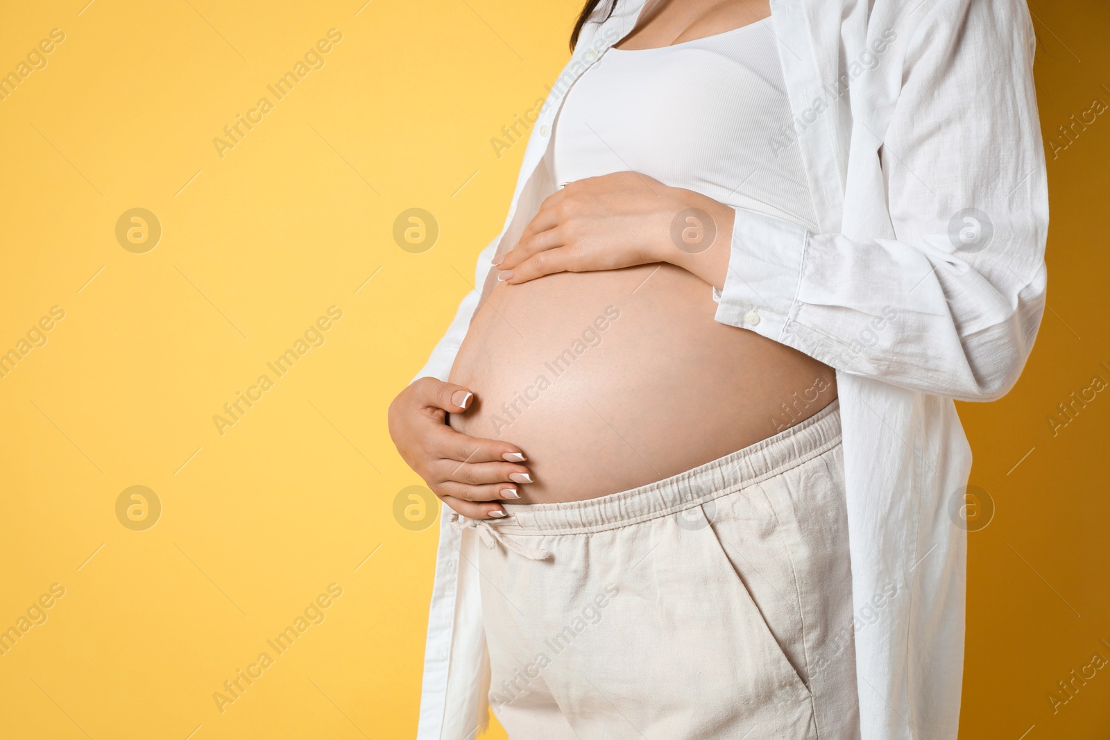 Photo of Young pregnant woman on yellow background, closeup. Space for text