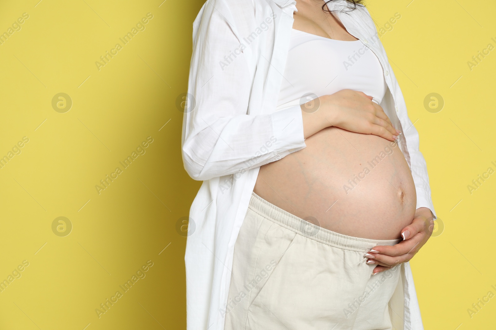 Photo of Young pregnant woman on yellow background, closeup. Space for text