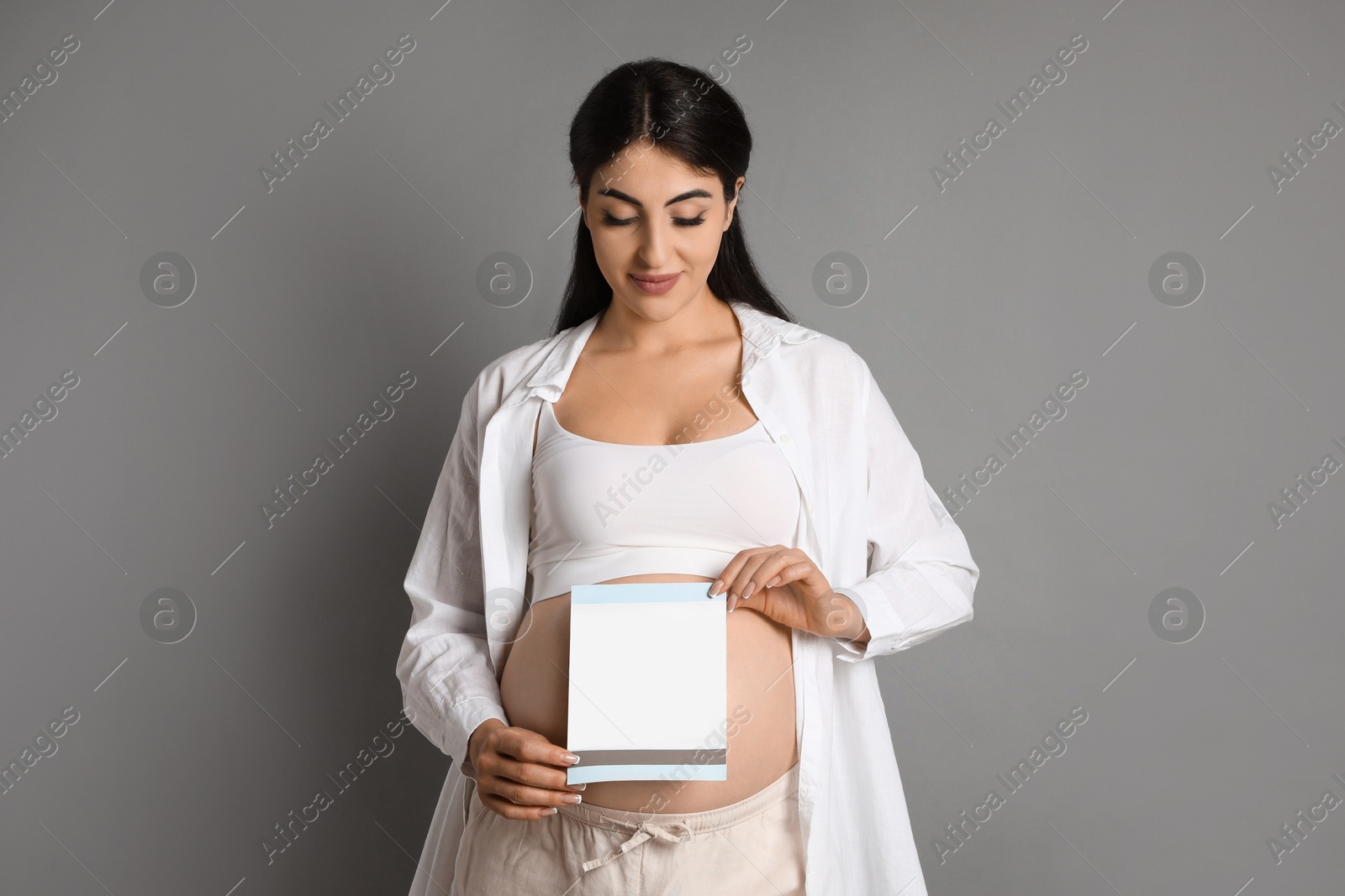 Photo of Portrait of beautiful pregnant woman with paper sheet on grey background