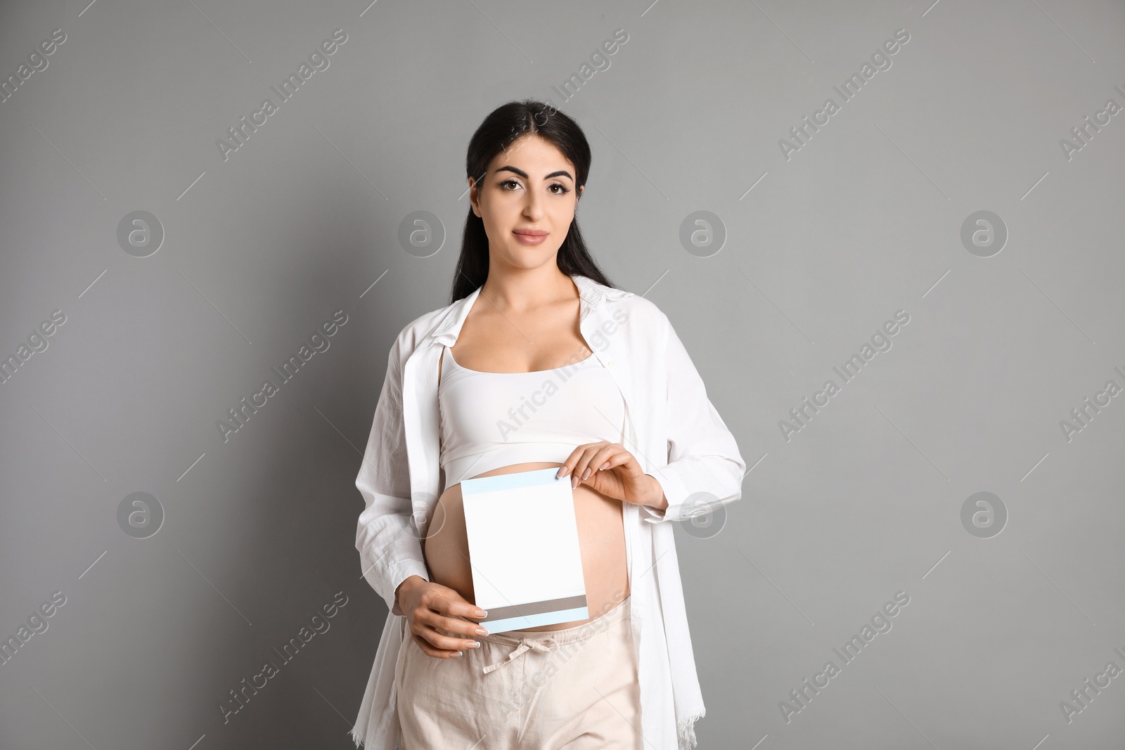 Photo of Portrait of beautiful pregnant woman with paper sheet on grey background