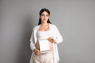 Photo of Portrait of beautiful pregnant woman with paper sheet on grey background