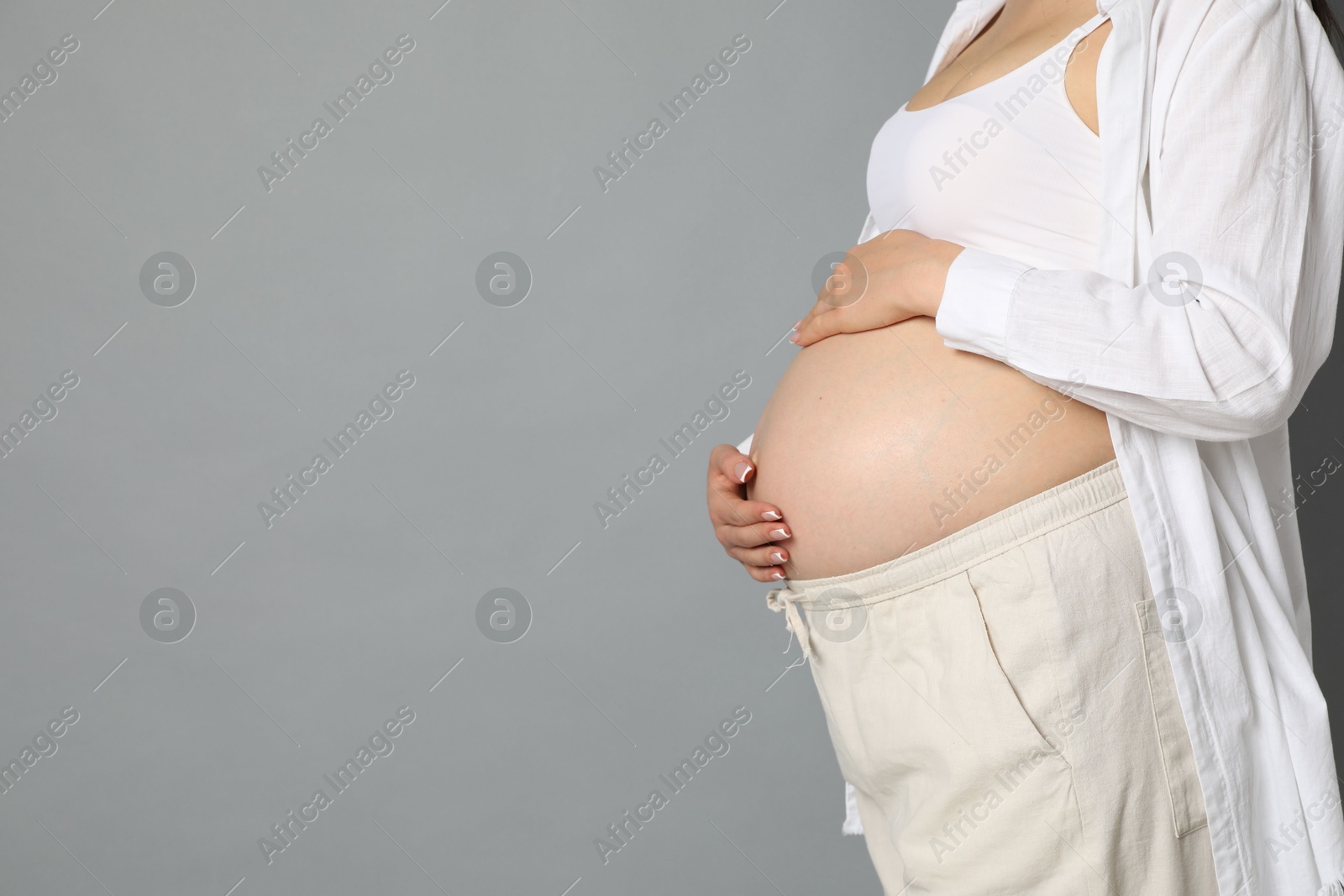 Photo of Young pregnant woman on grey background, closeup. Space for text