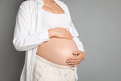 Photo of Young pregnant woman on grey background, closeup. Space for text