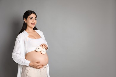 Photo of Portrait of beautiful pregnant woman with baby shoes on grey background, space for text