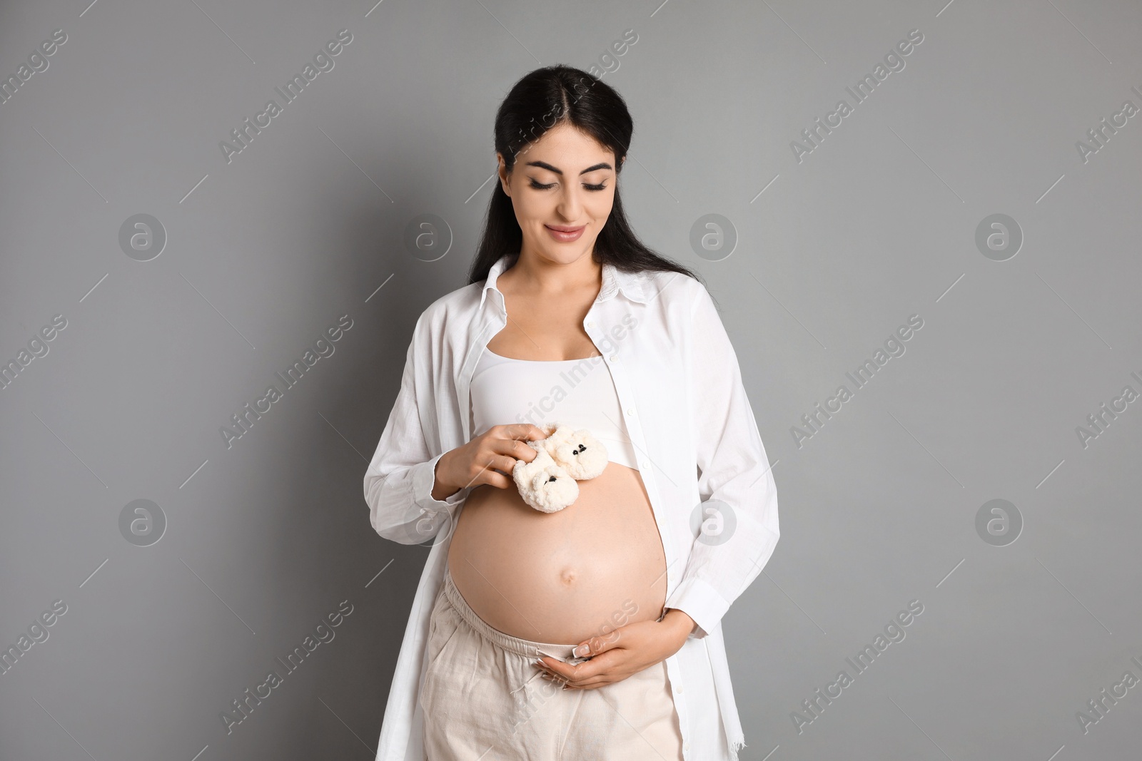 Photo of Portrait of beautiful pregnant woman with baby shoes on grey background