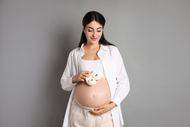 Photo of Portrait of beautiful pregnant woman with baby shoes on grey background