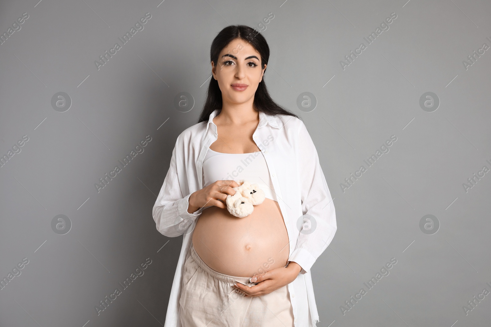 Photo of Portrait of beautiful pregnant woman with baby shoes on grey background