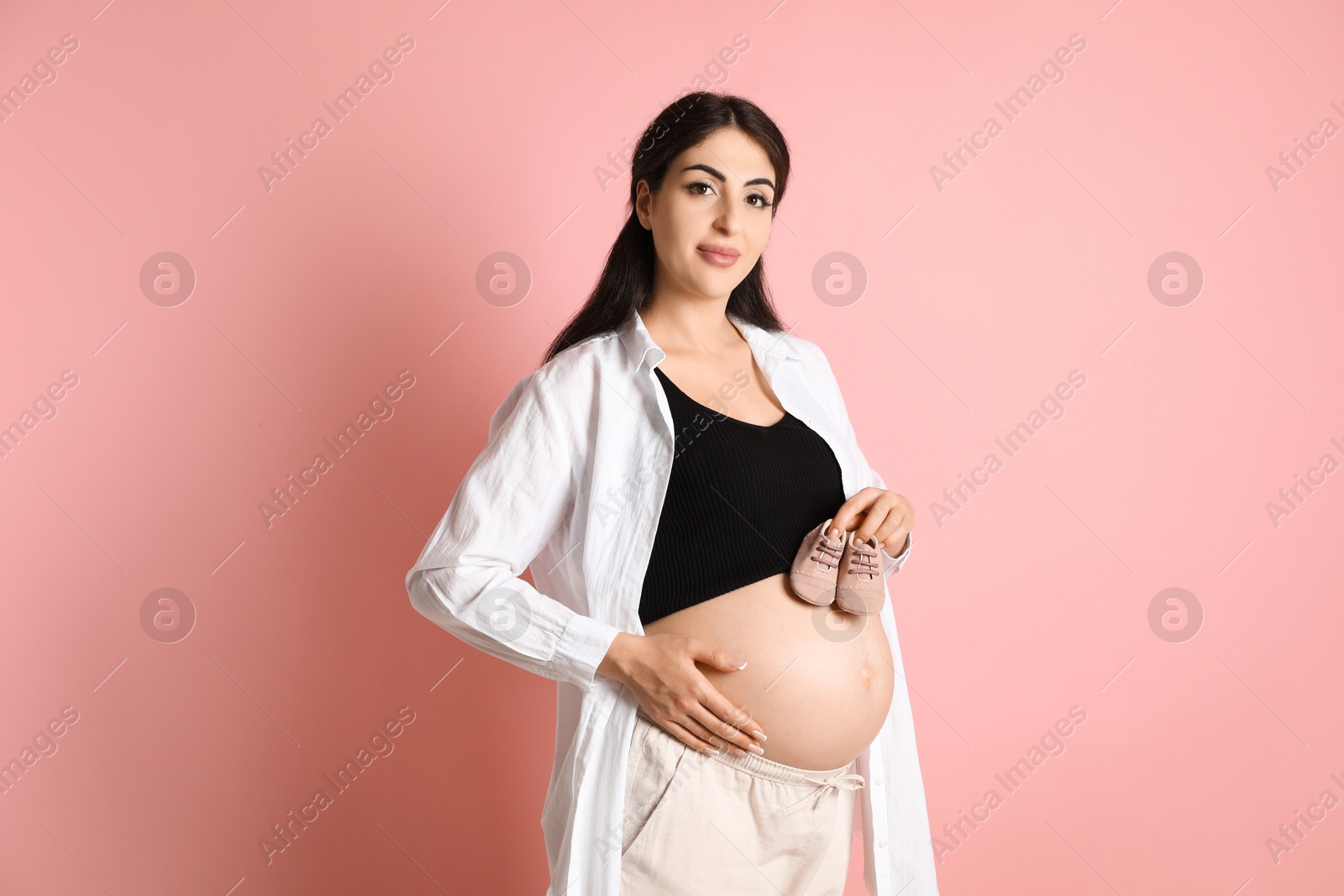 Photo of Portrait of beautiful pregnant woman with baby shoes on pink background